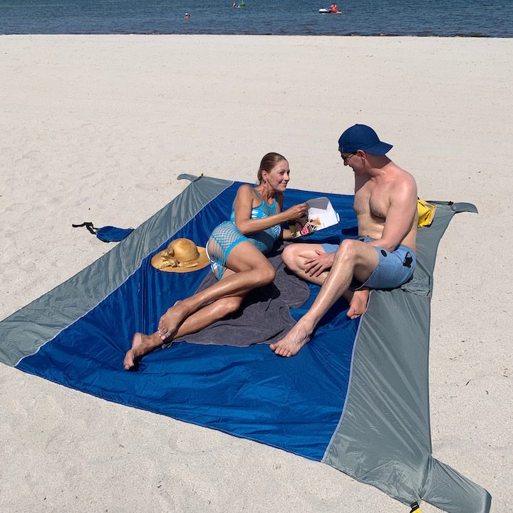 Two people on a dark blue SandStop blanket on the beach